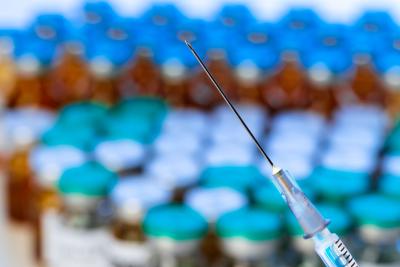 Close up of a needle of a syringe against pile of vials