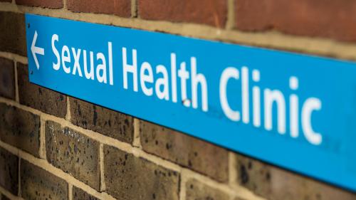 Blue sign on brick wall indication the direction to a Sexual Health Clinic
