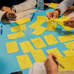 hands of people seating around a table writing on yellow post-its 