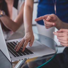 photo of hands working around a laptop on a glass table