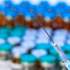 Close up of a needle of a syringe against pile of vials
