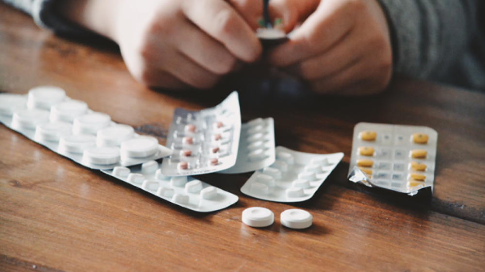 Hands removing differently coloured pills and tablets from packaging