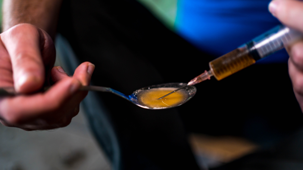 A hand holding a spoon with heroin and a syringe