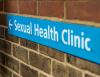 Blue sign on brick wall indication the direction to a Sexual Health Clinic